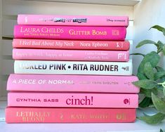 a stack of pink books sitting on top of a white shelf next to a potted plant