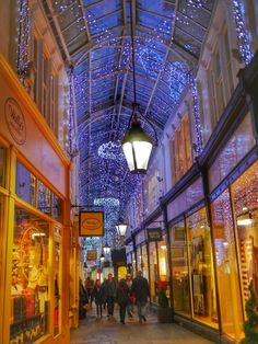 people are walking through an indoor shopping mall with lights on the ceiling and glass windows