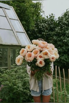 a woman holding a large bouquet of flowers in her hands while standing next to a greenhouse