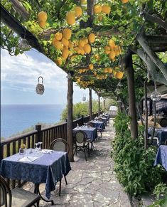 an outdoor dining area with tables and chairs overlooking the ocean on a sunny day, surrounded by greenery