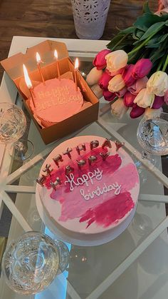 a birthday cake sitting on top of a glass table next to flowers and wine glasses