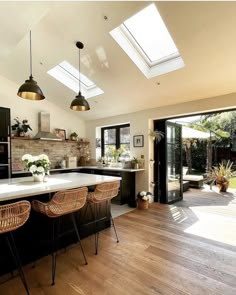 an open kitchen with wooden floors and skylights above the countertop, along with wicker bar stools