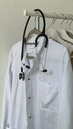 a doctor's coat and stethoscope hanging on a clothes rack in front of a white wall