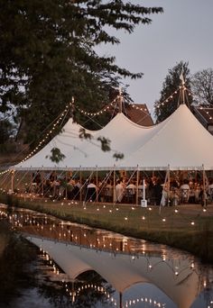 a large tent is set up next to the water with string lights strung around it