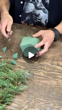 someone is making something out of paper on a wooden table with green leaves and grass