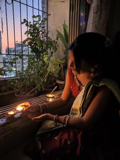 a woman sitting in front of a window holding a lit candle