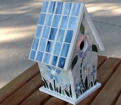 a birdhouse made out of stained glass sitting on a wooden bench