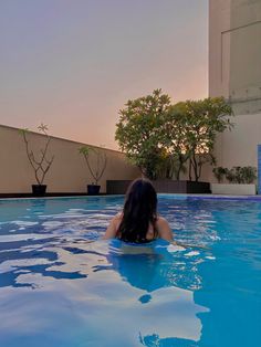 a woman is sitting in the middle of a swimming pool at sunset or dawn with her back turned to the camera