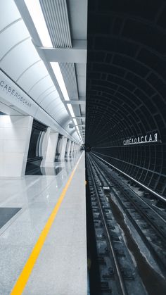 an empty subway station with yellow lines on the floor and black and white tiles on the walls