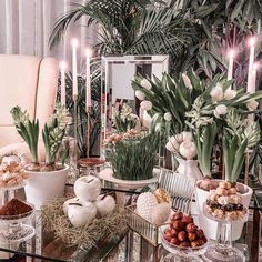 a glass table topped with lots of food and greenery next to a white chair