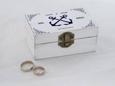 two wedding rings are sitting in front of a box with an anchor and cross on it