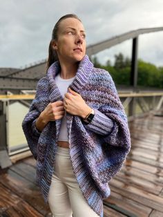 a woman standing on top of a wooden deck wearing a purple and blue knitted shawl