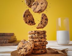 chocolate chip cookies falling into the air on top of a wooden board next to a glass of milk