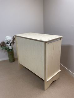 a white cabinet sitting next to a flower pot on the floor in a room with gray walls