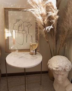 a marble table with two wine glasses on it next to a vase and some dried grass