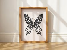 a black and white butterfly is in a wooden frame on the floor next to a wall