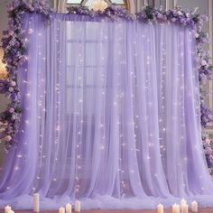 a purple backdrop with candles in front of it and some flowers on the back wall