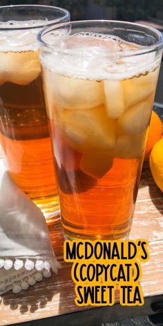 two glasses filled with ice tea sitting on top of a wooden table