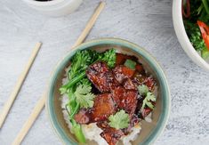 a bowl filled with meat and veggies next to chopsticks on a table