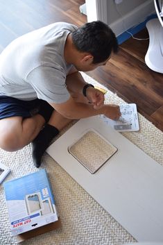 a man kneeling on the floor working on a piece of cardboard with scissors and tape