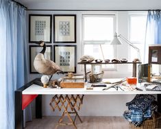 a white desk topped with lots of clutter next to a window covered in blue curtains