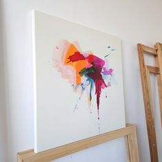 an abstract painting hangs on the wall next to a ladder and framed canvas with paint splattered onto it