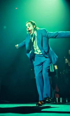 a man in a blue suit and tie on stage with his arms spread out to the side