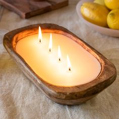 three lit candles in a wooden bowl on a table with lemons and a cutting board