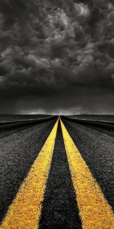 an empty road with two yellow arrows painted on it under a dark sky filled with clouds