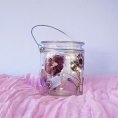 a glass jar filled with flowers sitting on top of a pink blanket