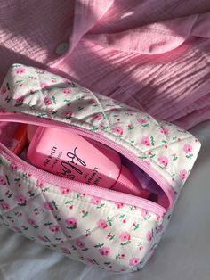 a pink and white floral bag with personal care items in it on top of a bed