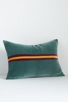 a green pillow sitting on top of a white bed next to a wall with a red and yellow stripe