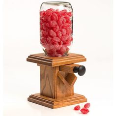 a jar filled with red candy sitting on top of a wooden stand next to two pieces of fruit