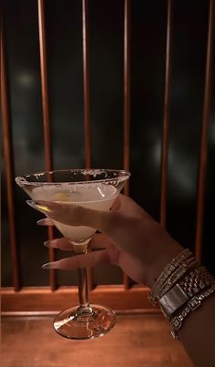 a hand holding a martini glass in front of a railing