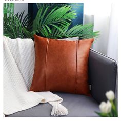 a brown pillow sitting on top of a gray couch next to a green palm tree