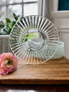 two glass dishes sitting on top of a wooden cutting board next to a pink flower