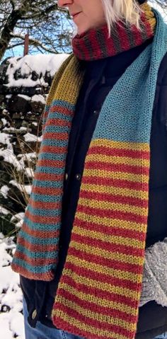 a woman standing in the snow wearing a multicolored knitted scarf and hat