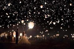 the bride and groom are surrounded by lanterns in the night sky at their wedding reception