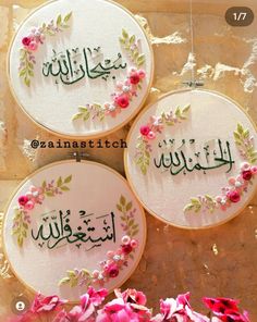 three embroidered hoops with arabic writing on them and flowers in front of a stone wall