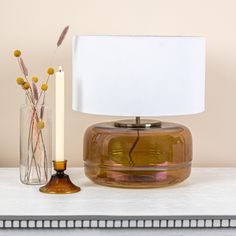 a table with a lamp, vase and flowers on it next to a candle holder