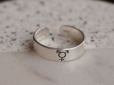 Everyone deserves to be represented, so if you identify as transgender, show your pride with this minimalist ring. Product Details: Materials: Sterling Silver, Fine Silver, or Gold Filled Color: Silver or Gold Size: 6mm You will receive one hand-stamped ring filled with a black enamel finish. Transgender Symbol, Gender Expression, Stamped Ring, Hand Stamped Ring, Meaningful Design, Stamped Rings, Minimalist Ring, Minimalist Rings, Beautiful Ring