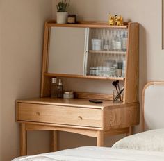 a wooden desk with a mirror on top of it next to a white bed in a room