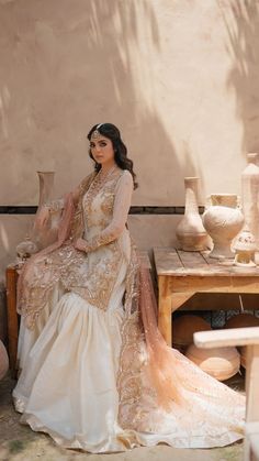 a woman sitting on top of a wooden bench wearing a white and gold dress with sheer sleeves