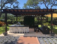 an outdoor kitchen with bar stools and tables in the middle of a garden area