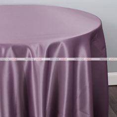 a round table covered with a purple satin tablecloth and white wall in the background