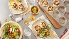 an assortment of appetizers and salads on trays next to muffin tins