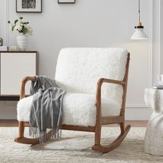 a white rocking chair with a blanket on it in front of a table and pictures