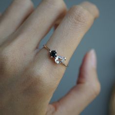 a woman's hand holding a ring with two stones on it and the middle one has a black diamond