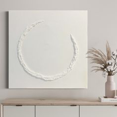 a vase with flowers on top of a wooden table next to a white wall mounted art piece