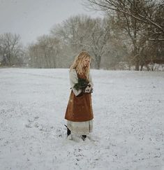 a woman is standing in the snow holding flowers